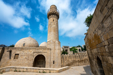 Exterior view of the Shirvanshah Palace Mosque in Baku Azerbaijan showing stone domes and arches of the historic complex under a clear blue sky.