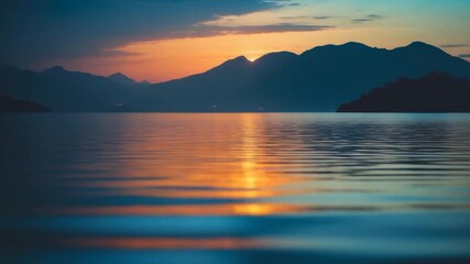 Wide view of calm lake at sunset with vibrant orange and blue reflections on the water surface mountains silhouetted against the colorful sky smooth ripples in the foreground - Powered by Adobe