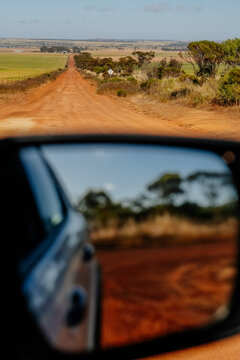Car side mirror reflection and red dirt road