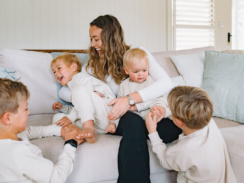 Mum sitting on the couch cradling her two sons while older brothers tickling their feet