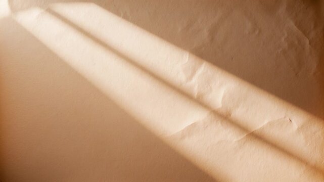Soft natural light casting shadows across a textured beige paper background transitioning from varied tones as sunlight shifts highlighting subtle creases and smooth surfaces.