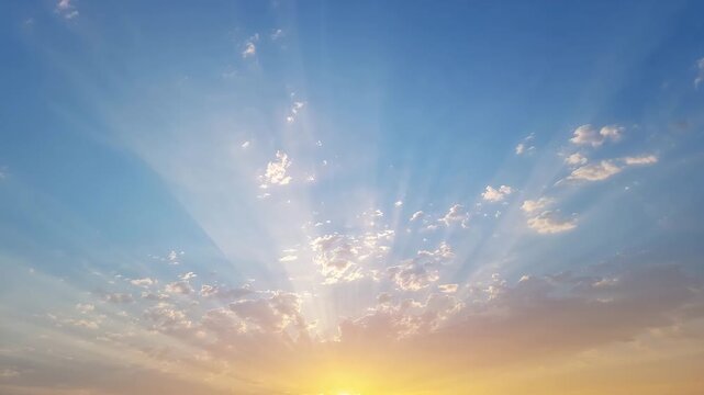 Wide view of a vibrant sunrise over the horizon with soft clouds golden rays breaking through the clear blue sky showcasing the transition of light from dawn to daytime.