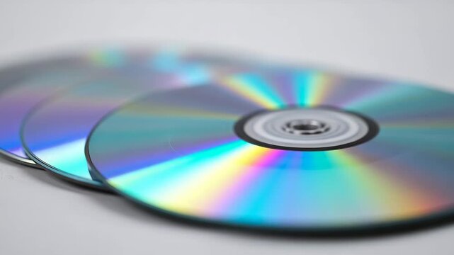 Close-up of multiple shiny CDs stacked on a white background showcasing their reflective surfaces and rainbow-like colors highlighting intricate details and textures throughout the scene