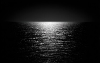 Serene black and white seascape, reflecting bright light across the rippled water