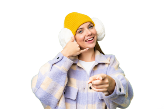 Young blonde woman wearing winter muffs over isolated chroma key background making phone gesture and pointing front