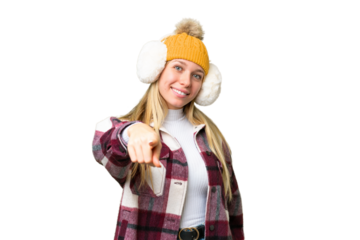 Young pretty blonde woman wearing winter muffs over isolated chroma key background points finger at you with a confident expression