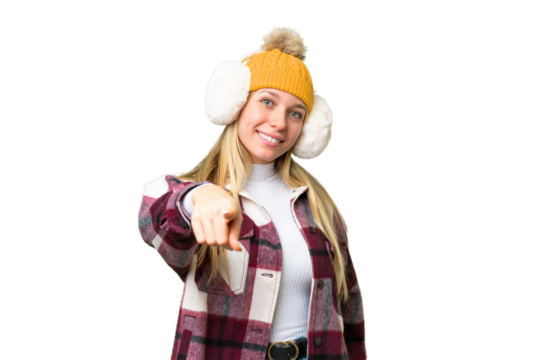 Young pretty blonde woman wearing winter muffs over isolated chroma key background points finger at you with a confident expression