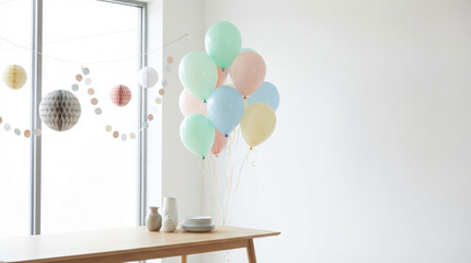 Pastel colored balloons and honeycomb decorations hang near a wooden table with plates and vases in a bright room