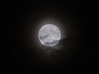 Glowing full Moon shines brightly in the dark Night Sky with a soft atmospheric Halo around it, captured from Earth.