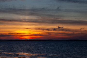 a deep red golden orange blue sunset over the North Sea with streaks of grey and dark grey clouds, England, UK