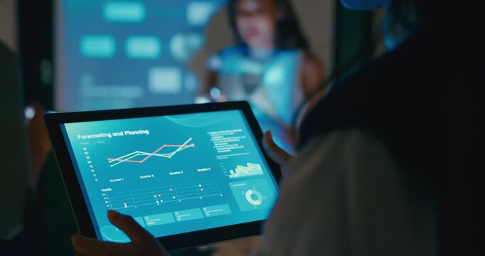 Close up group Asian businesspeople work together leads business meeting uses presentation TV with profit sale statistics in office night. Financial generation z team brainstorm on e-Commerce project.