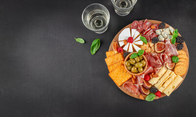 Elegant charcuterie board with assorted cheeses, cured meats, crackers, olives, figs, berries and wine on dark background with copy space