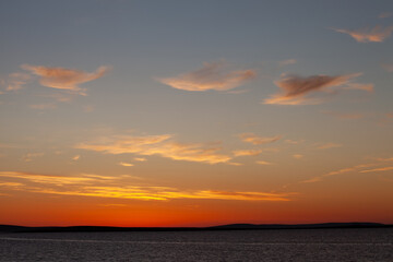 landscape of pale blue sky with red golden lit clouds at sunset during midsummer on the island of Stronsay, Orkney Islands, Scotland, UK