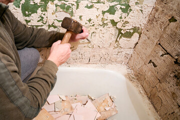 Bathroom renovation. A worker knocks down old ceramic tiles in the bathroom with a hammer and chisel.