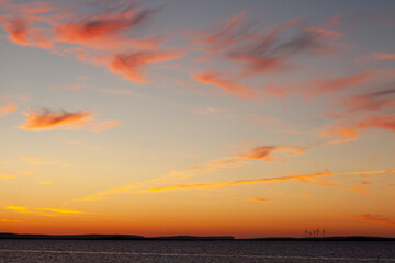 vast pale blue and pink orange sky of sunset during midsummer and on the horizon is the distant detail of wind turbines of community wind farm in the Orkney Islands, Scotland, UK