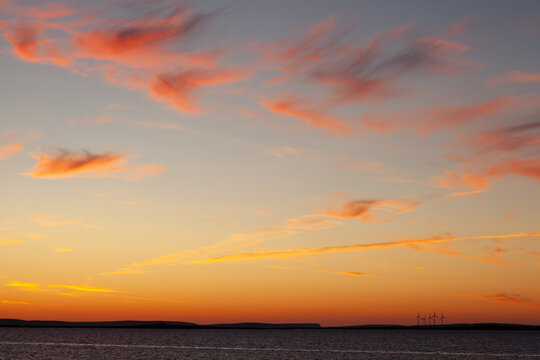 vast pale blue and pink orange sky of sunset during midsummer and on the horizon is the distant detail of wind turbines of community wind farm in the Orkney Islands, Scotland, UK