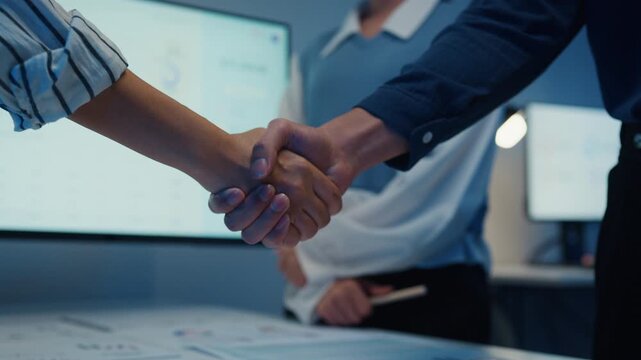 Close up multiracial group young Asia businesspeople in smart casual wear discussing business shaking hand together while stand in modern night office. Partner cooperation, coworker teamwork concept.