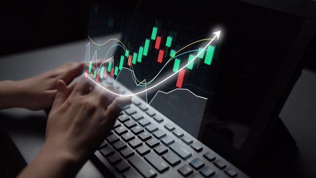 A close-up of hands typing on a laptop while displaying a financial chart on the screen, featuring green and red candlesticks and an upward trend line against a dark backdrop. Copula