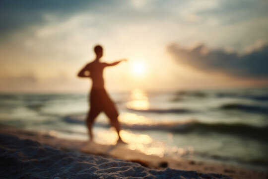 Blurred man stretching on sandy beach at sunrise, ocean waves in background, peaceful and energetic atmosphere, early morning exercise, healthy lifestyle, silhouette