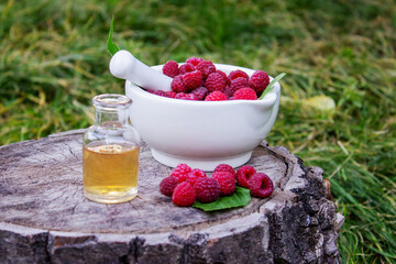 Fresh raspberries in a mortar with a bottle of natural herbal extract or essential oil outdoors.