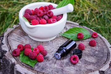 Fresh raspberries in a mortar with a bottle of natural herbal extract or essential oil outdoors.