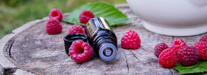 Fresh raspberries in a mortar with a bottle of natural herbal extract or essential oil outdoors.