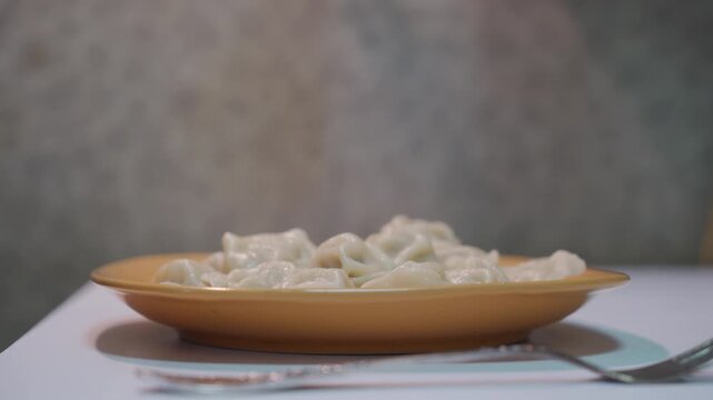 Hot meat dumplings fill the yellow square plate on the white table. A silver fork lies nearby as the fresh savory meal steams, ready to be enjoyed for dinner.