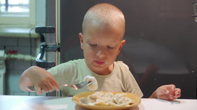Hot meat dumplings with sour cream fill the yellow plate on the table. The hungry child is holding a silver fork to eat the savory pastry, sticking his tongue out in anticipation.