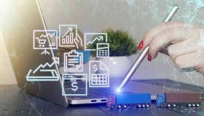 Futuristic concept of logistics and e-commerce featuring a hand using a stylus on a laptop, digital business icons, and toy trucks.