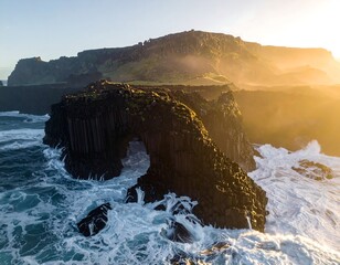 Aerial view of coastal rock formation with ocean waves at sunset