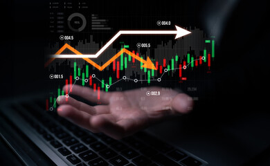 A business professional analyzing stock market trends using digital tools while projecting data through a hand above a laptop, showcasing investment strategies and market insights. Scalp