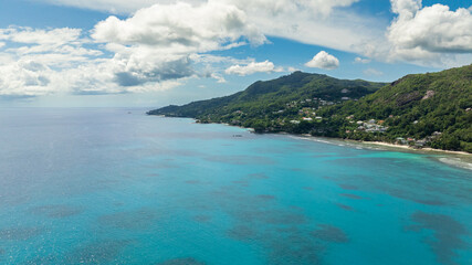 Fototapeta premium Coastal stretch with turquoise waters and green forested hills, small homes nestled within. Seychelles, Mahe.