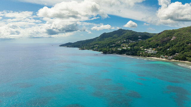 Coastal stretch with turquoise waters and green forested hills, small homes nestled within. Seychelles, Mahe.