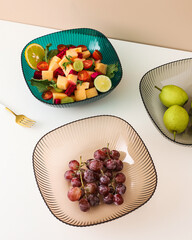 Aesthetic arrangement of fresh fruit salads pears and grapes in colorful glass bowls on white table