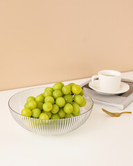 Fresh bunch of shine muscat green grapes in glass bowl with cup of tea on beige background