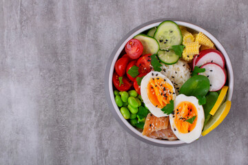 Poke bowl with smoked redfish, eggs, vegetables, edamame beans and rice served on gray table. Healthy balanced meal with white fish. Top view, copy space