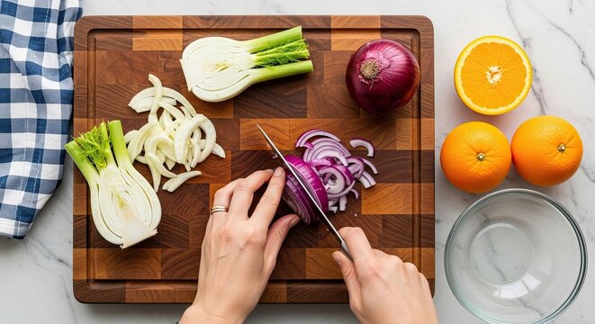 A person's hands slice a fresh red onion with a knife on a wooden cutting board next to sliced fennel and oranges, a top-down view of healthy meal preparation on a marble surface - Powered by Adobe