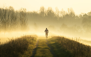 Samotny biegacz na polnej drodze w gęstej, złotej mgle o wschodzie słońca