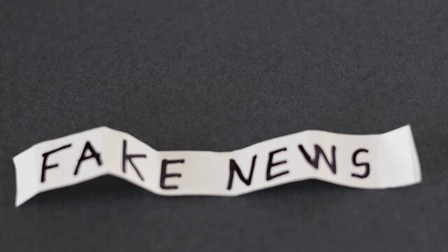 Un primer plano de un papel de color blanco con las palabras noticias falsas con movimiento en un fondo gris oscuro