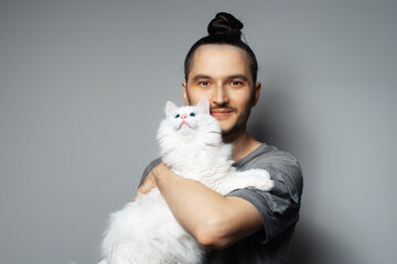Studio portrait of young man with white cat in arms on grey background. Pet with blue eyes.