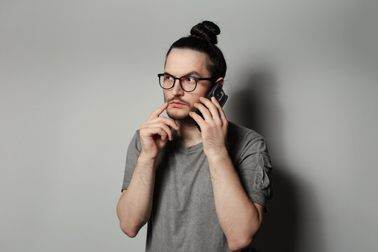 Studio portrait of young serious man talking on smartphone on grey background.
