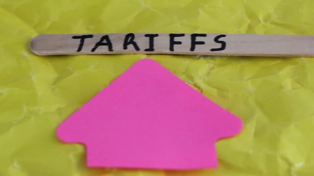 Un primer plano de una paleta de madera con la palabra de aranceles y una flecha de color rosado con movimiento en un fondo amarillo. Pol&iacute;tica econ&oacute;mica 