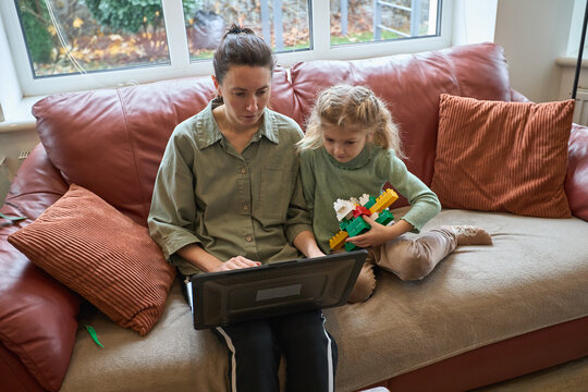 Mother and child bonding time with laptop and building blocks on cozy couch