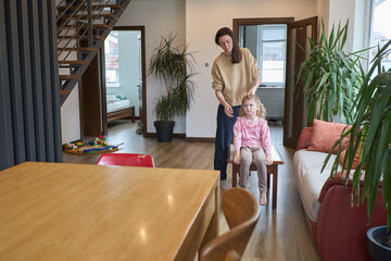 Mother brushing daughter's hair in cozy modern home living room