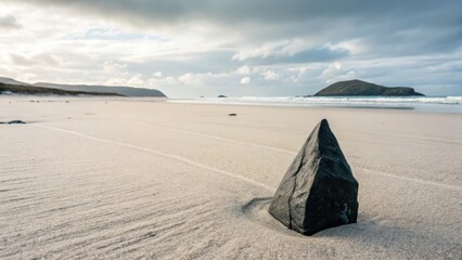 A solitary dark rock rests on a vast, sunlit sandy beach with rolling ocean waves and distant hills under a cloudy sky.