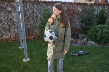 Young girl holding soccer ball in backyard garden next to skateboard