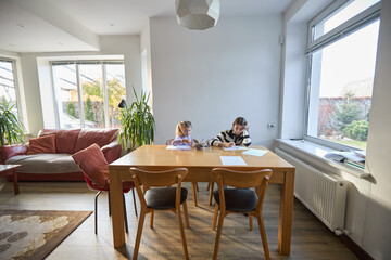 Children studying at table in modern, bright living room