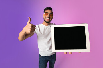 A cheerful young Arab man is presenting a tablet with an empty screen, giving a thumbs up while suggesting a new application or website. The colorful neon background enhances the vibe.