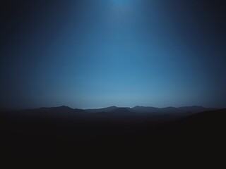 Obraz premium A dramatic mountain range silhouette against a beautiful blue gradient sky creates an atmospheric and serene background, perfect for nature themes and conveying mystery.