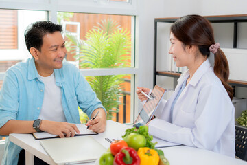 Asian nutritionist using tablet to explaining personalized meal plan with AI to patient during healthcare consultation, healthy lifestyle, woman dietitian showing nutrition plan with AI on tablet.